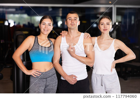 Positive young man and two girls posing together in gym Positive young man and two girls posing together in gym 117794060