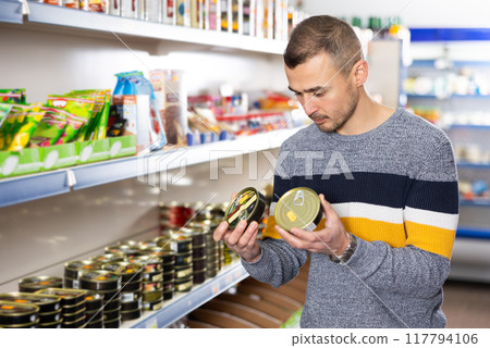 In Russian goods store, man choose canned sprats in oil In Russian goods store, man choose canned sprats in oil 117794106