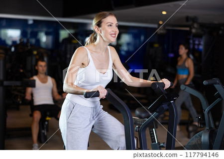 Sportive young girl doing air bike exercises in well-equipped gym 117794146