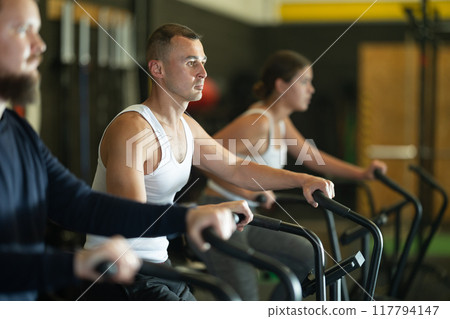 Man doing cardio workout on air bike during group training in gym Man doing cardio workout on air bike during group training in gym 117794147
