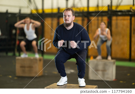 Sportive young guy squatting on box during crossfit workout Sportive young guy squatting on box during crossfit workout 117794160