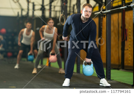 Bearded guy performing one arm kettlebell swings in gym Bearded guy performing one arm kettlebell swings in gym 117794161