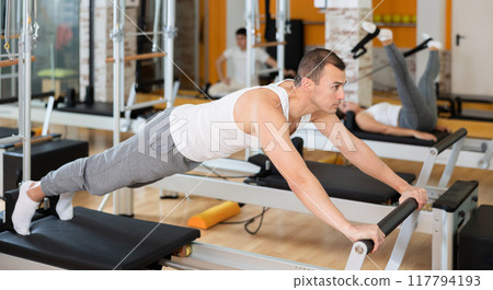 Man in different poses performs static and dynamic exercises on reformer 117794193