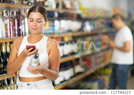 Girl using smartphones to scan barcodes on bottles of alcoholic 117794223