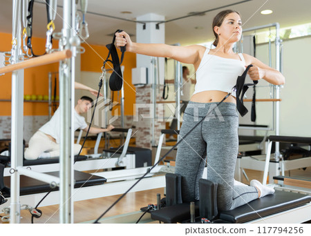 Girl performing pulling straps exercise on Pilates reformer 117794256