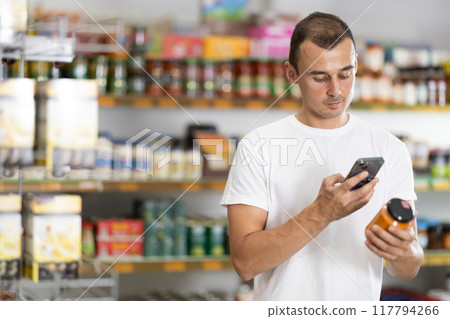 Male shopper scanning barcode or qr code with smartphone on canned food label 117794266