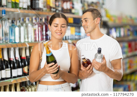 Married couple chooses alcoholic drinks in supermarket - vodka, champagne or whiskey 117794270