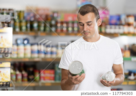 Young man choosing canned food in store Young man choosing canned food in store 117794303