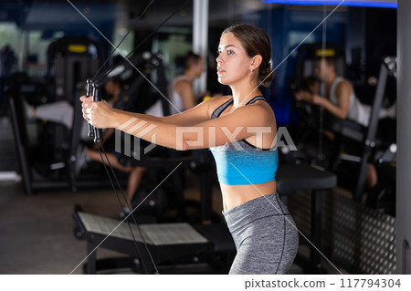 Active athlete young woman during exercises on crossover exercise machine with loops and weighting Active athlete young woman during exercises on crossover exercise machine with loops and weighting 117794304