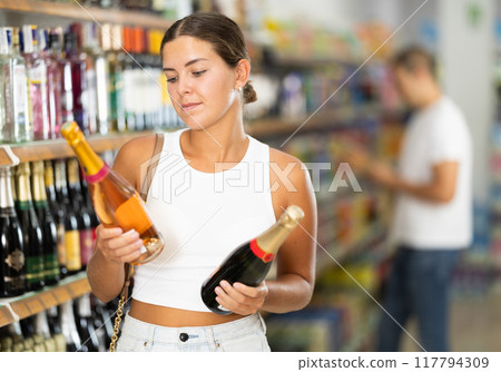 Woman chooses bottle of champagne in shop store 117794309