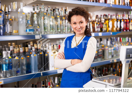 Portrait of positive saleswoman at cash register of liquor store Portrait of positive saleswoman at cash register of liquor store 117794322