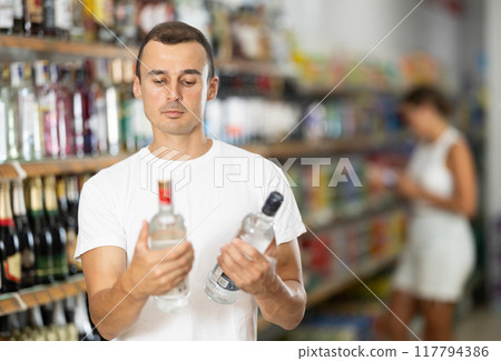 Male buyer chooses bottle of vodka in supermarket 117794386