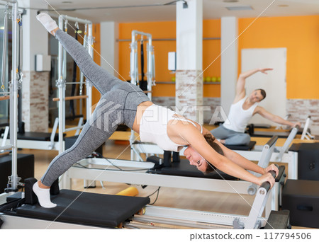 Girl doing exercises on Pilates reformer in fitness studio Girl doing exercises on Pilates reformer in fitness studio 117794506