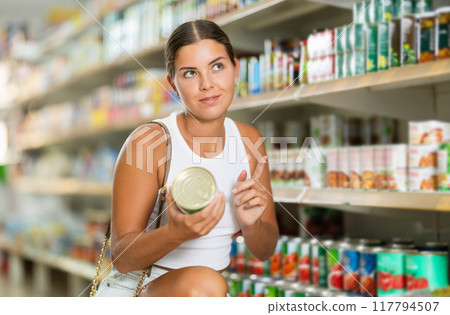 Young woman chooses canned food in store 117794507