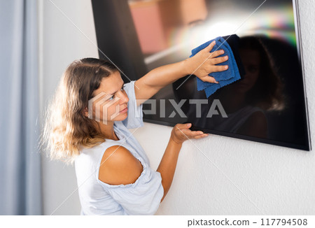 Housewife wipes dust from the TV at home with rag 117794508