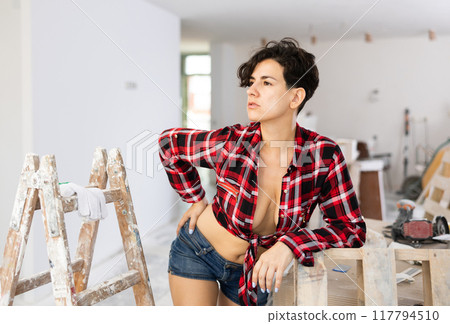 Sexy girl in plaid shirt and shorts posing in cottage under construction Sexy girl in plaid shirt and shorts posing in cottage under construction 117794510