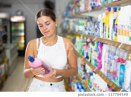 Woman carefully selects cleaning product in industrial section of supermarket Woman carefully selects cleaning product in industrial section of supermarket 117794549