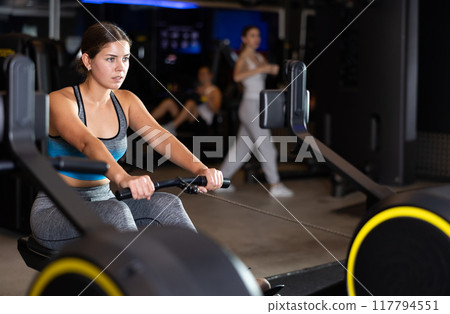 Sportive young girl training on cable row machine in gym Sportive young girl training on cable row machine in gym 117794551