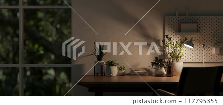 A wooden desk by the window in a room at nighttime, illuminated by a table lamp. A wooden desk by the window in a room at nighttime, illuminated by a table lamp. 117795355