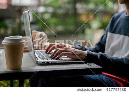 A close-up side view image of a man working remotely from an outdoor table, using his laptop. A close-up side view image of a man working remotely from an outdoor table, using his laptop. 117795388