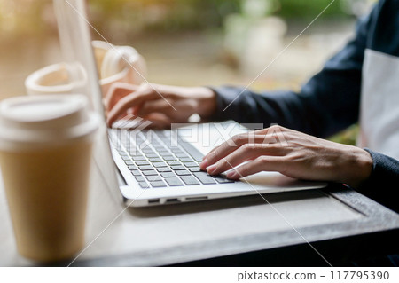 A close-up side view image of a man working remotely from an outdoor table, using his laptop. 117795390