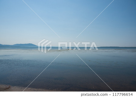 A calm scene of a large lake. Birds are resting in the shallow water. 117796654