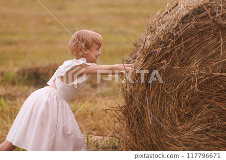 Young girl cheerfully pushing a haystack 117796671