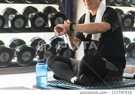 Athlete looking at watch at gym, working out, man making body, exercise, interval 117797916