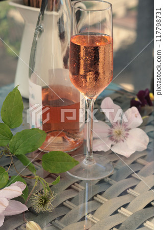 Rose wine and flowers on terrace on sunny day. Drinks of Mediterranean. Wicker furniture in garden, summer and vacation. Rose wine and flowers on terrace on sunny day. Drinks of Mediterranean. Wicker furniture in garden, summer and vacation. 117798731