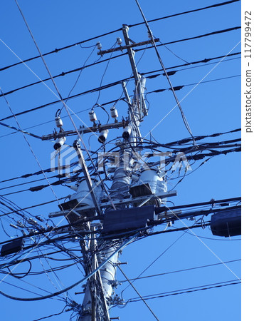 A telegraph pole with a tangle of wires and blue sky A telegraph pole with a tangle of wires and blue sky 117799472