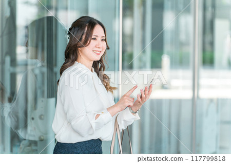 Business woman using smartphone in building (apps, video viewing, SNS, music, search, news, e-books, side job) 117799818