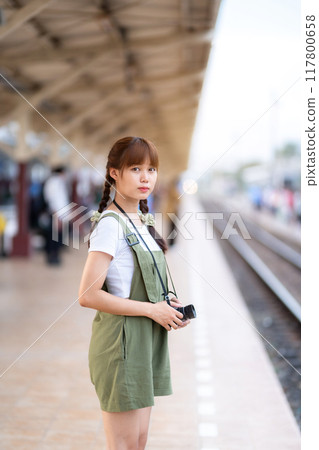 Portrait Young asian woman smiling tourist Traveler girl walking and with a holding the camera waits train travel journey is taken in railway platform Thailand, summer relax vacation Concept. Portrait Young asian woman smiling tourist Traveler girl walking and with a holding the camera waits train travel journey is taken in railway platform Thailand, summer relax vacation Concept. 117800658