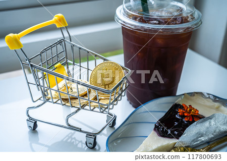 Close-up of Golden bitcoins or cryptocurrency coin or symbols in shopping cart and Americano iced coffee or black and Blueberry Cake in white table. Future currency concept. Close-up of Golden bitcoins or cryptocurrency coin or symbols in shopping cart and Americano iced coffee or black and Blueberry Cake in white table. Future currency concept. 117800693
