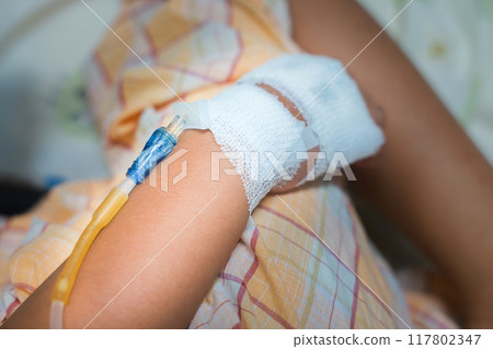 Close up child hand with tube of normal saline infusion at the hospital because it is influenza A. Hand of a patient in Hospital ward. Concept about treatment, emergency, medical, chemotherapy, sick. Close up child hand with tube of normal saline infusion at the hospital because it is influenza A. Hand of a patient in Hospital ward. Concept about treatment, emergency, medical, chemotherapy, sick. 117802347