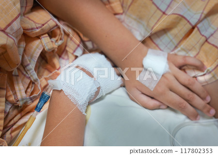 Close up child hand with tube of normal saline infusion at the hospital because it is influenza A. Hand of a patient in Hospital ward. Concept about treatment, emergency, medical, chemotherapy, sick. 117802353