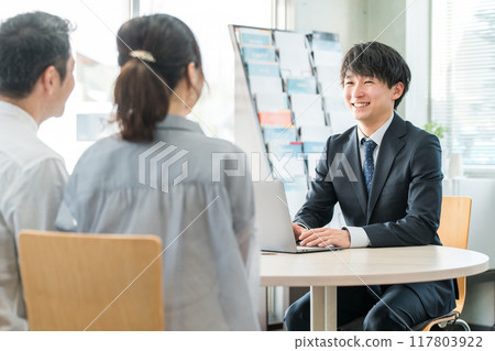 一位年輕的亞洲商人和一對客戶夫婦在陳列室/商務談判空間為客戶提供服務 117803922