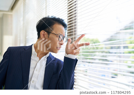 一個男人透過百葉窗往外看 117804295