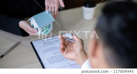 Real Estate Agent and Buyer Reviewing Contract with House Model Real Estate Agent and Buyer Reviewing Contract with House Model 117804945