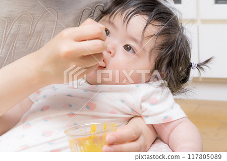 [Baby with tied hair eating baby food] 117805089
