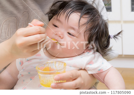 [Baby with tied hair eating baby food] 117805090