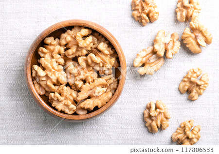 Walnut kernel halves in a wooden bowl on linen fabric. Shelled and dried halves of walnut kernels, ripe seeds of common walnut tree Juglans regia, used as snack or for baking. Close-up from above. 117806533