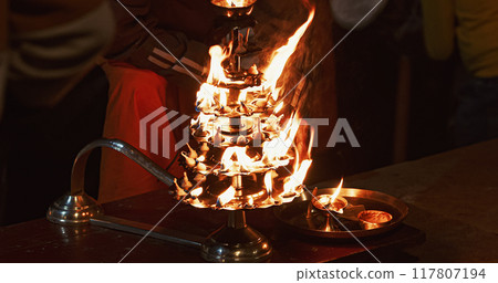 Varanasi, Uttar Pradesh, India. Candle Holder With Lit Candles On Ganga Maha Aarti Ceremony Begins. Fire Puja Ritual In Varanasi. Traditional Ganga Aarti At Ghat Varanasi, Uttar Pradesh, India. Candle Holder With Lit Candles On Ganga Maha Aarti Ceremony Begins. Fire Puja Ritual In Varanasi. Traditional Ganga Aarti At Ghat 117807194