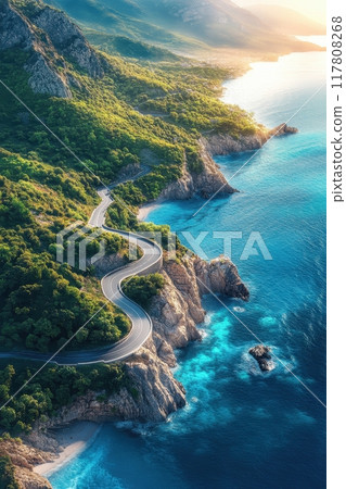 Aerial View of a Serpentine Coastal Road Winding Through Lush Green Hills Along a Turquoise Blue Ocean 117808268