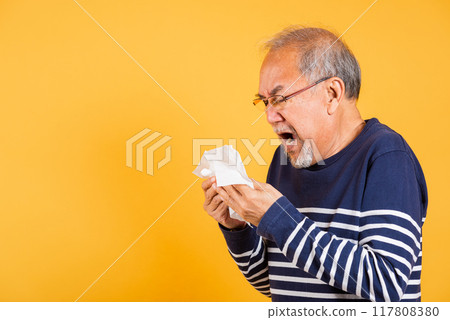 Asian elder man cold having flu and sneezing from sickness virus problem use tissue studio shot isolated on yellow background, Portrait senior old man blowing nose with tissue, pensioner unwell 117808380