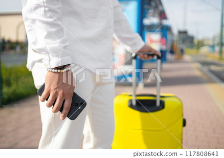 Close-up of male Caucasian hand holding travel bag near bus stop. Unrecognizable young man arriving at hotel. Unknown client entering room with luggage. Travelling, tourism, business trip, lifestyle. 117808641
