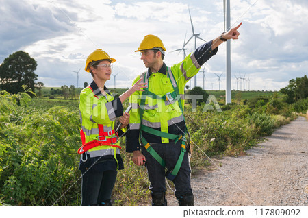 Two men in safety gear are pointing at a wind farm 117809092