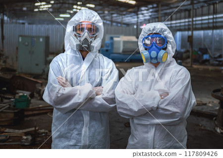 Two people in white protective gear are standing in front of a building Two people in white protective gear are standing in front of a building 117809426
