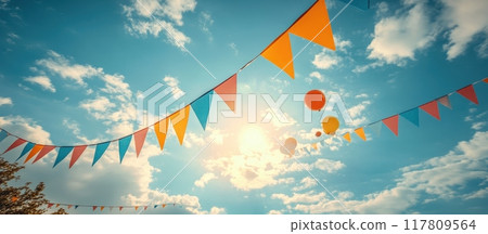 Colorful Festive Bunting Flags and Balloons Against a Bright Blue Sky with Fluffy Clouds on a Sunny Day 117809564