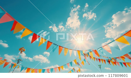 Colorful Festive Bunting Flags Against a Bright Blue Sky with Sunlight and Fluffy Clouds Colorful Festive Bunting Flags Against a Bright Blue Sky with Sunlight and Fluffy Clouds 117809601