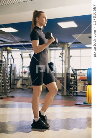 Woman exercising with dumbbells in a well-equipped gym during the day Woman exercising with dumbbells in a well-equipped gym during the day 117810667